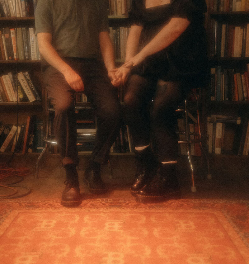 A couple sitting stools holding hands.