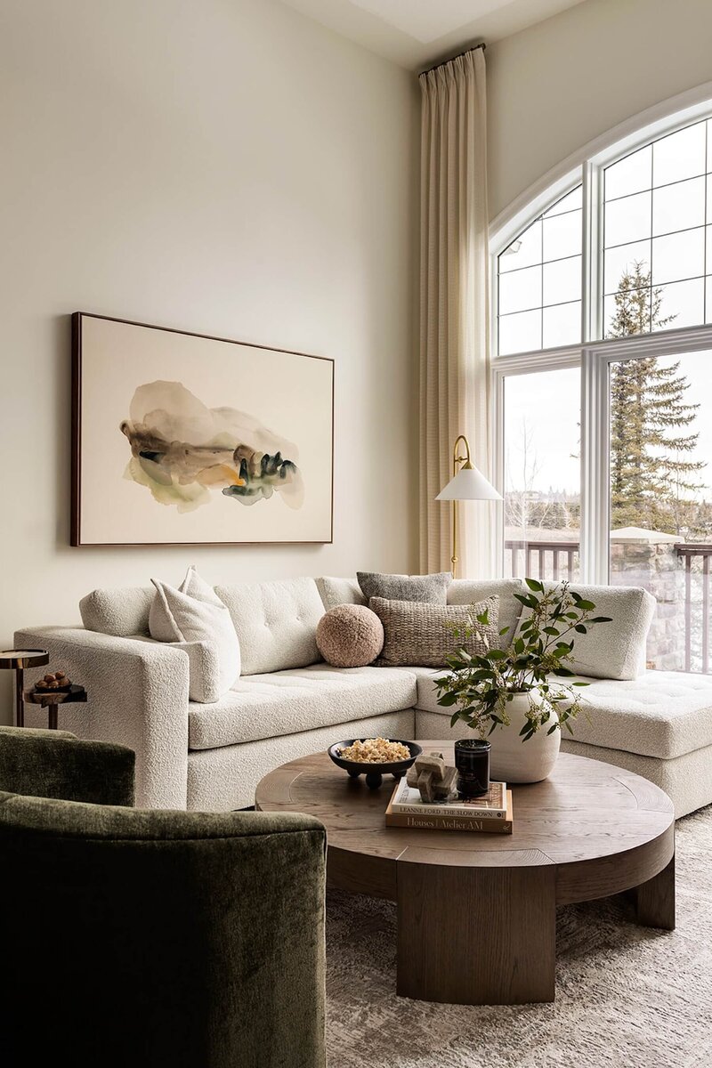 Custom living room sectional with abstract neutral artwork and round wooden coffee table with hints of green. 