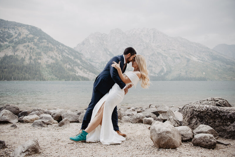 wyoming elopement with bride and groom at Jenny Lake as the groom dips his bride backwards and leans his forehead into her with the moutnains onthe other side of the lake that was behind them