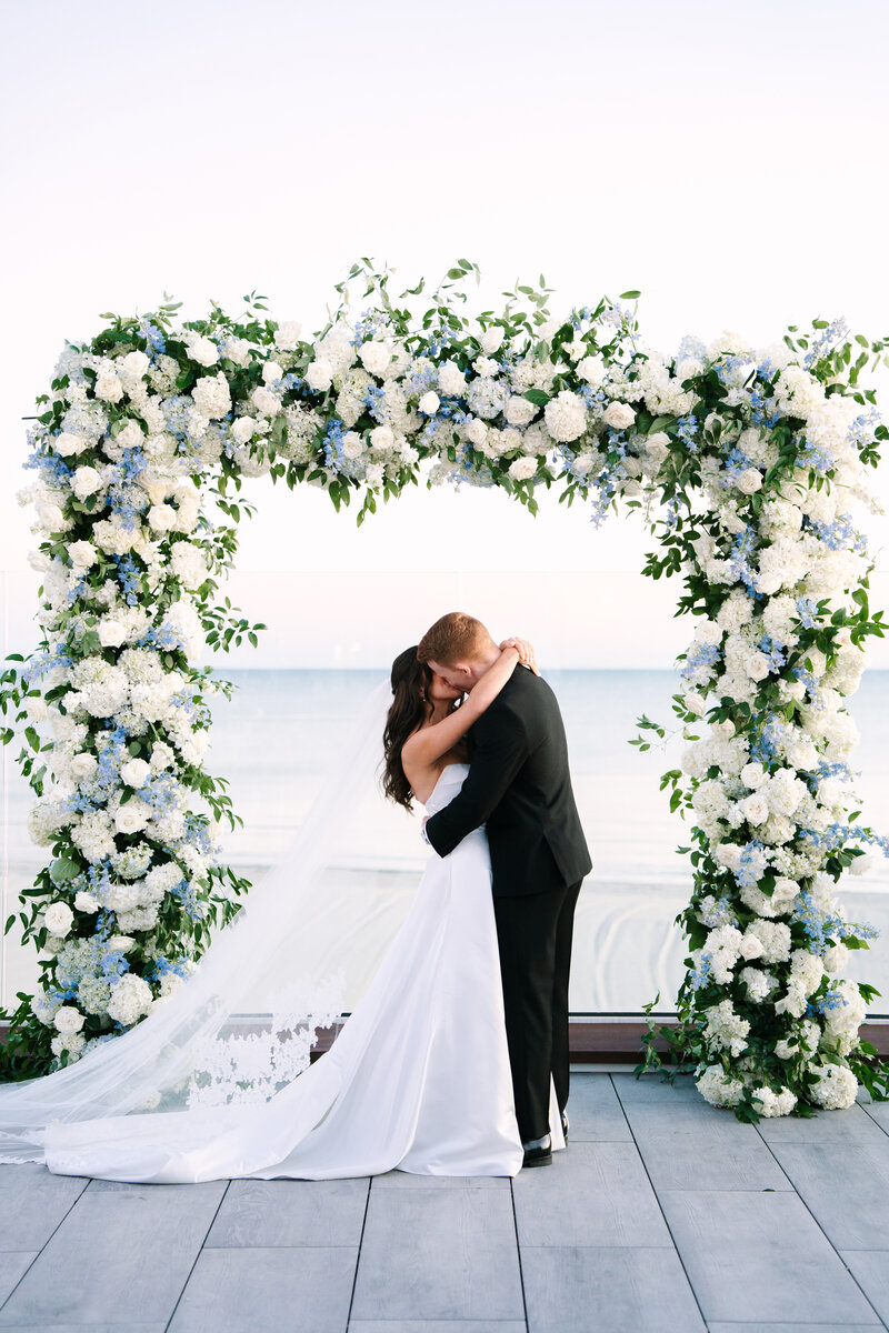 bride and groom kissing underneath a floral arch during their Wychmere Dune Cape Cod wedding ceremony