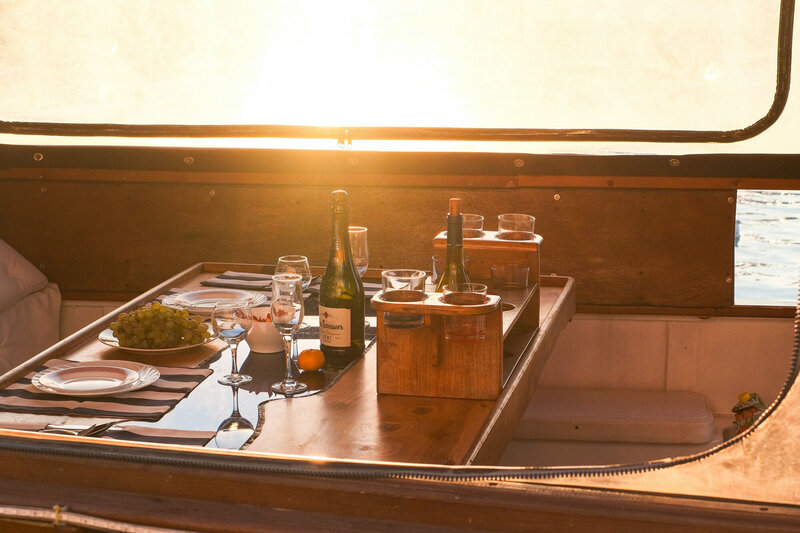A sunset dining setting on a yacht with a table set with wine glasses, a bottle of champagne, and an appetizer plate