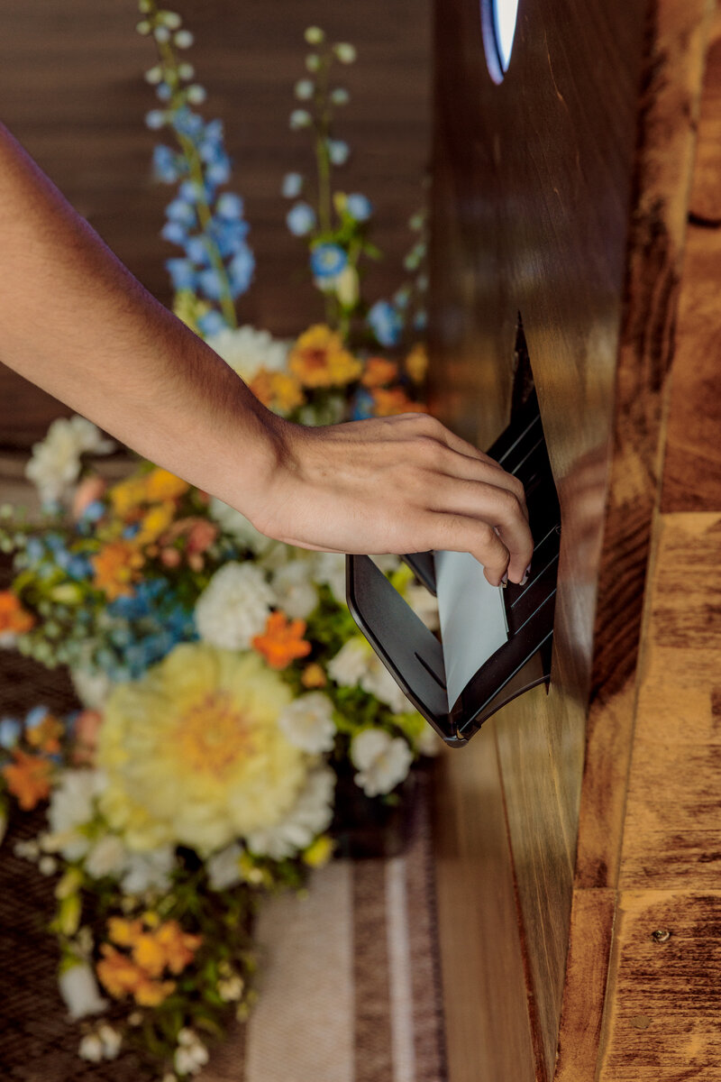 bride takes photo strips from the printer of the photo booth with colorful florals in the background