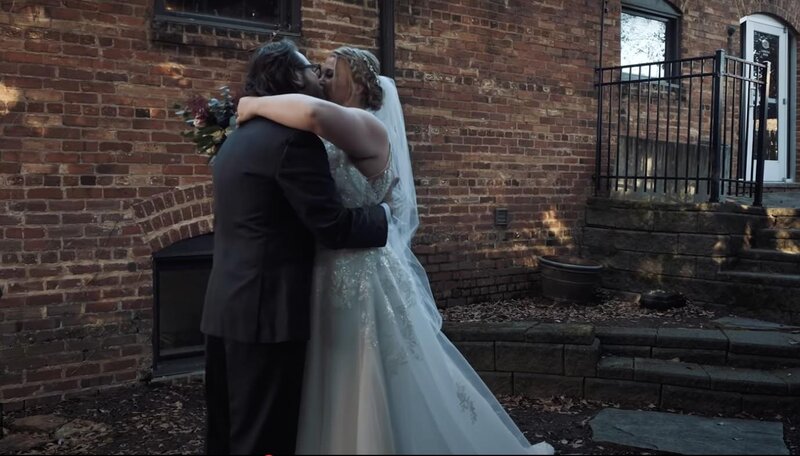 A newlywed couple kissing in front of a brick building 
