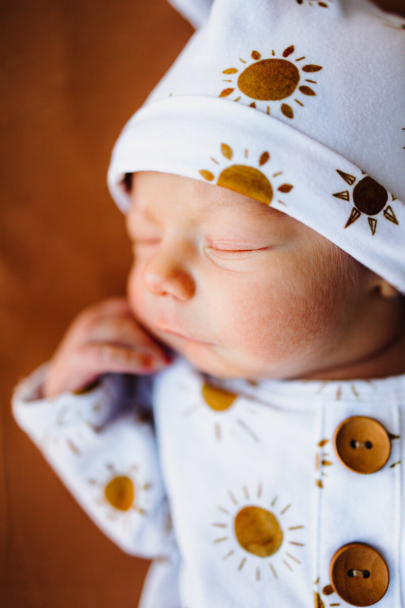 Newborn Photography Tutorial featuring a peacefully sleeping baby boy on a table. He's dressed in a complete outfit with a white cap and pajamas adorned with small sun patterns.