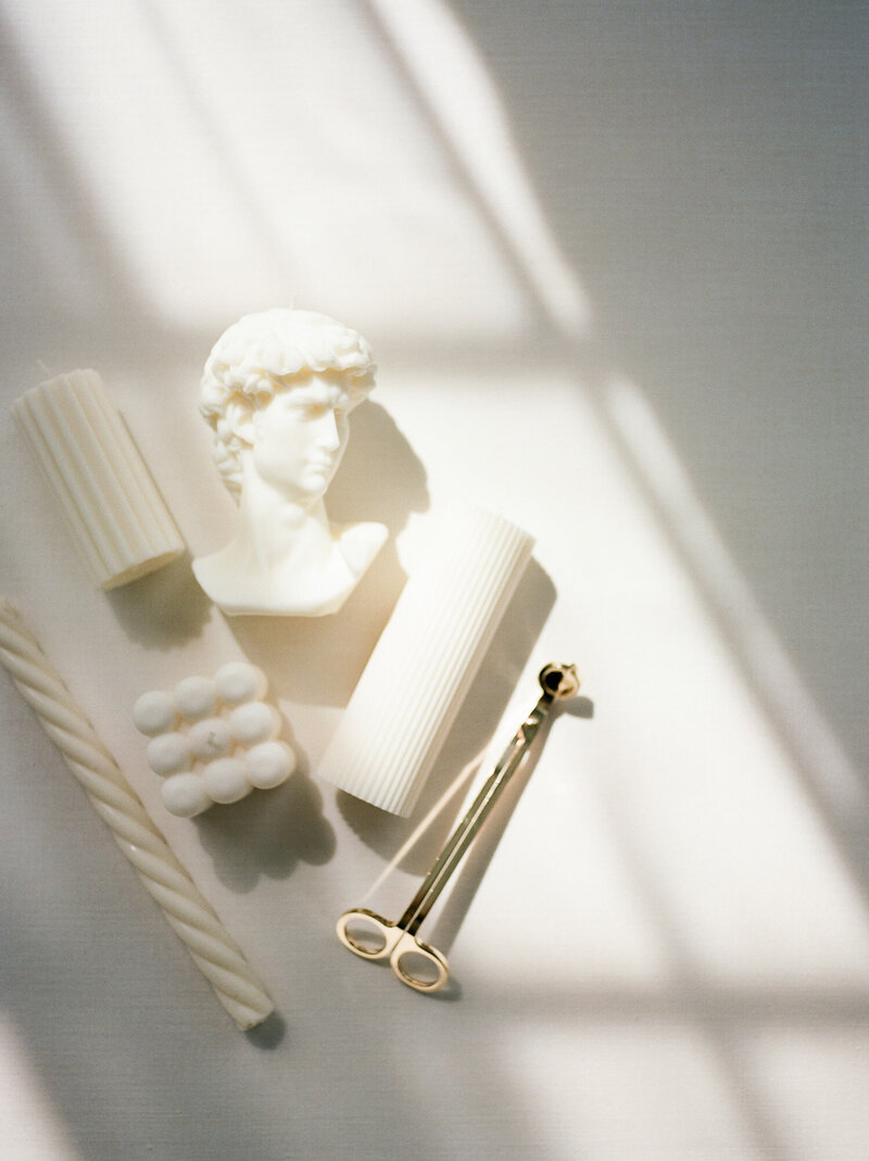 ethereal film flat lay with directional light, sculptural ivory candles, brass wick trimmer