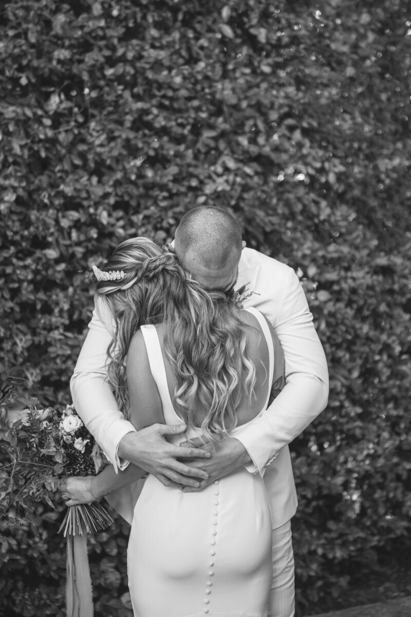 A groom embraces his bride in a heartfelt first look, captured in a timeless black and white moment.