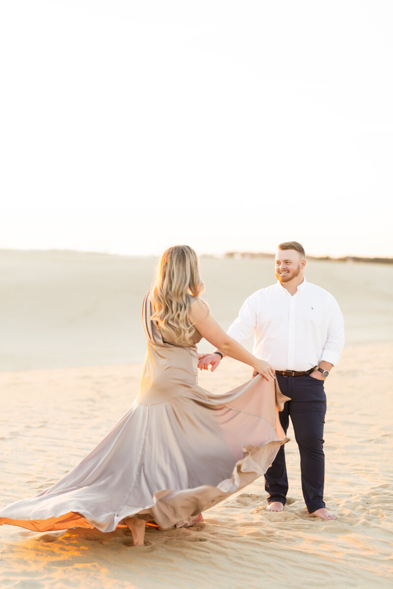 A couple dances barefoot in the golden dunes at sunset, the bride’s flowing gown catching the light in a magical, cinematic moment