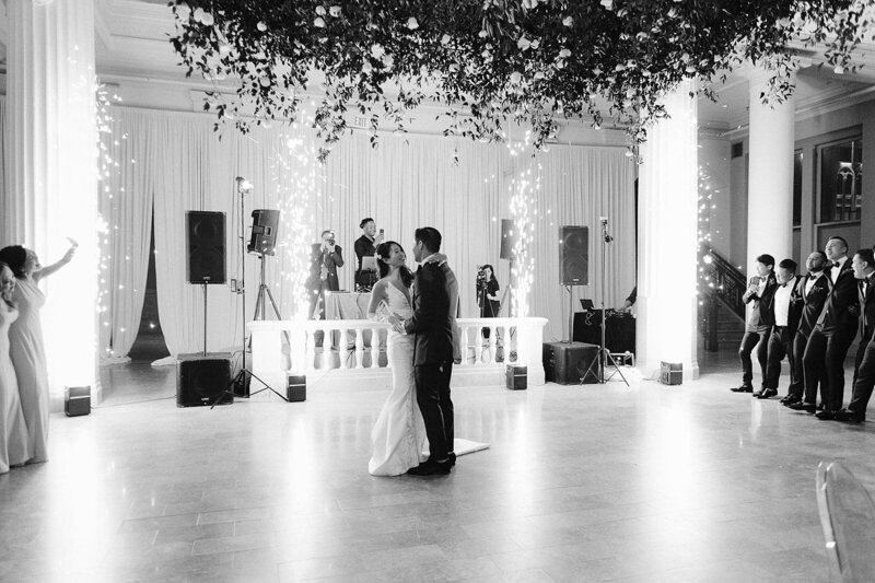 Black and white photo of bride and groom dancing at their reception with sparklers in the background