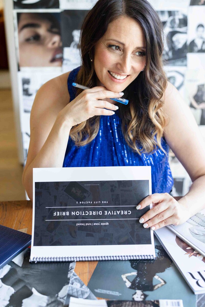 Brand strategist in sparkling royal blue top dress reviewing creative direction brief while sharing authentic smile