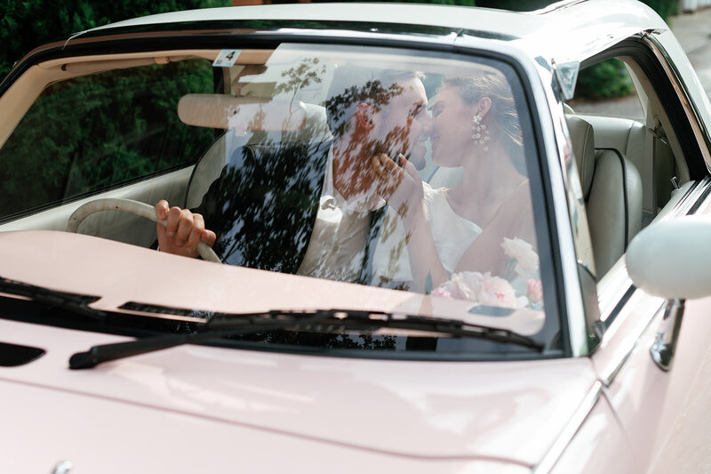  Bride and groom smiling in their getaway car outside Laguna Gloria, surrounded by classic garden architecture.