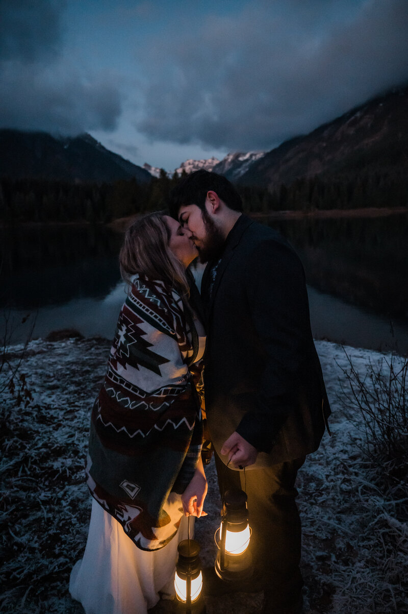 Bride and groom holding lanterns and kissing during their winter elopement day at Gold Creek Pond in Washington State