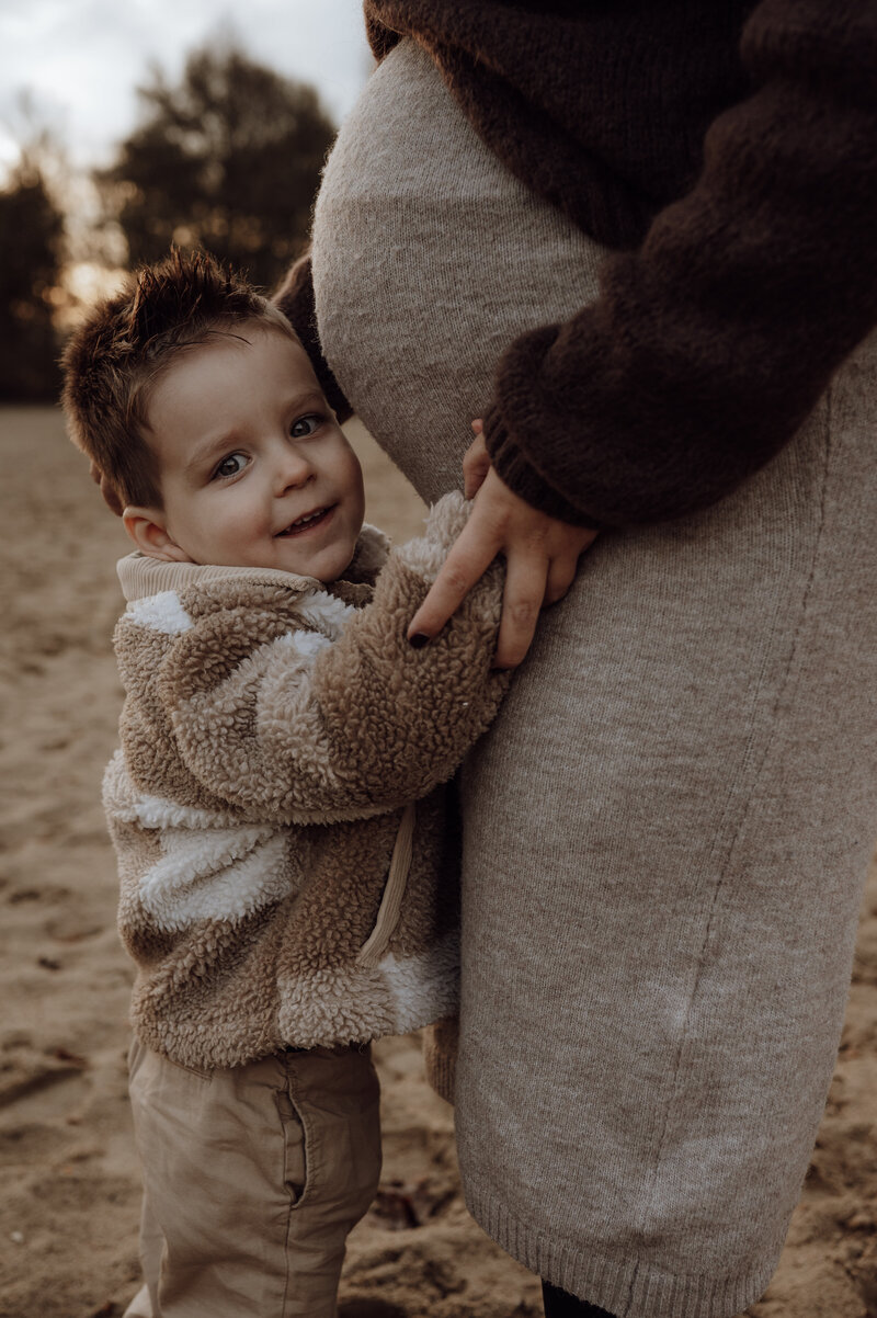 Zoontje houdt zwangere buik van mama vast tijdens zwangerschapsshoot in Antwerpen