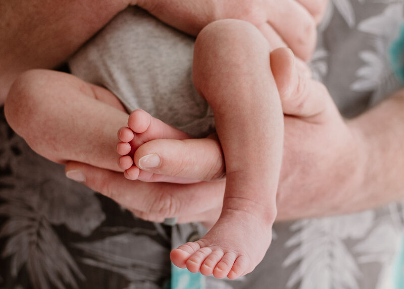Detailed newborn photo with dad holding baby's feet in his hand in lifestyle stuido.