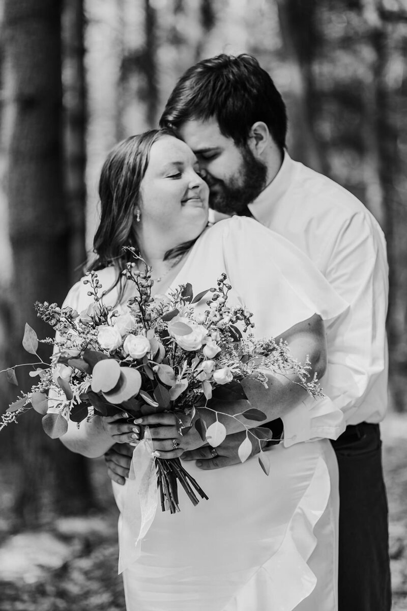 Groom embraces his bride at wooded elopement