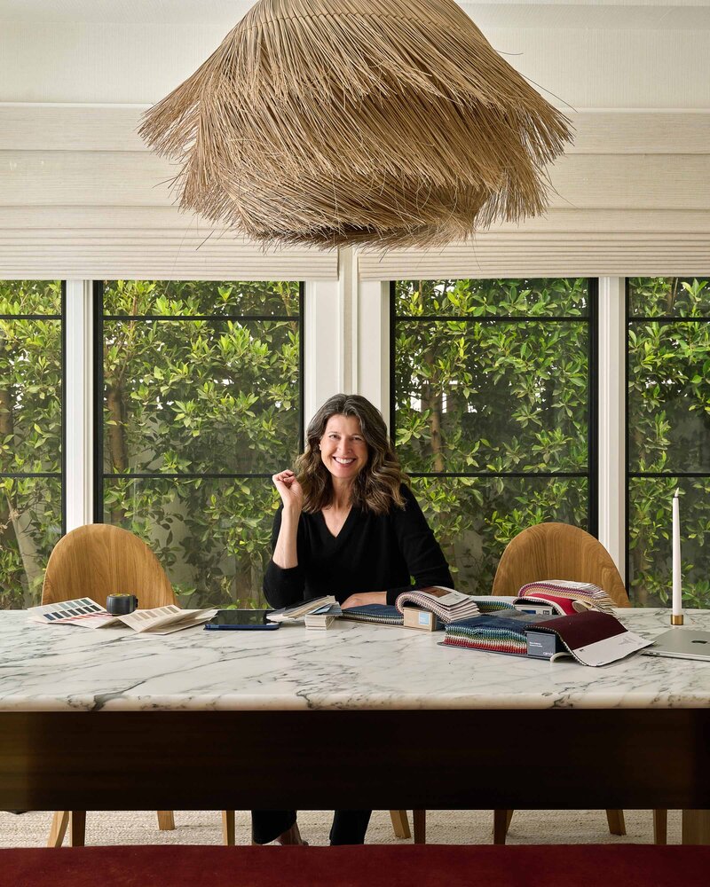Designer & Art Consultant, Laura Ford, sitting at a desk with fabric and paint swatches