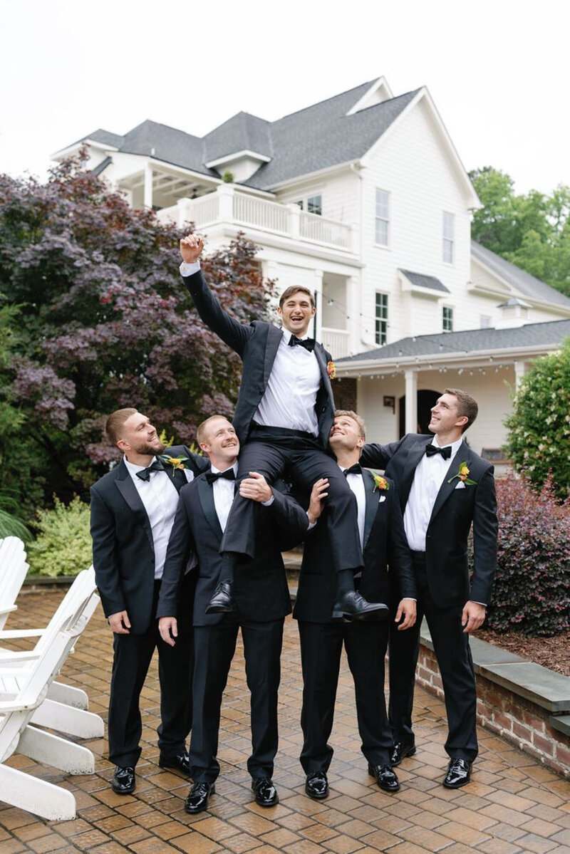 Groomsmen holding groom up in the air outside Raleigh wedding