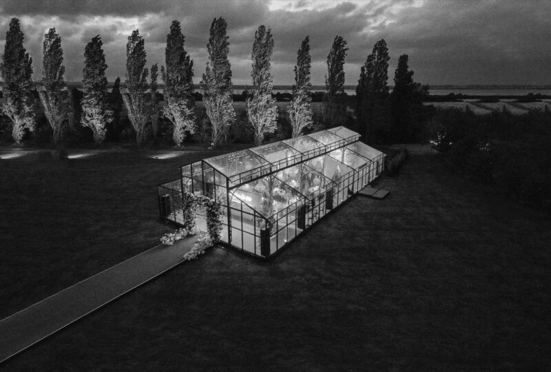An aerial view of a glass marquee on a lawn with a long walkway and flowers at the entrance for Amelia and Olly Murs