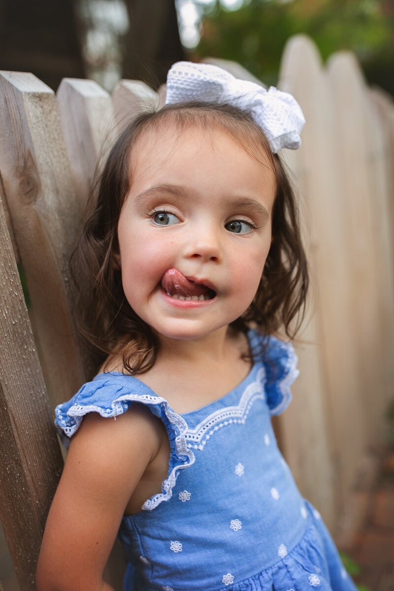 young-girl-in-blue-dress-making-a-funny-face-and-licking-her-lips-during-a-playful-outdoor-photoshoot-in-indianapolis