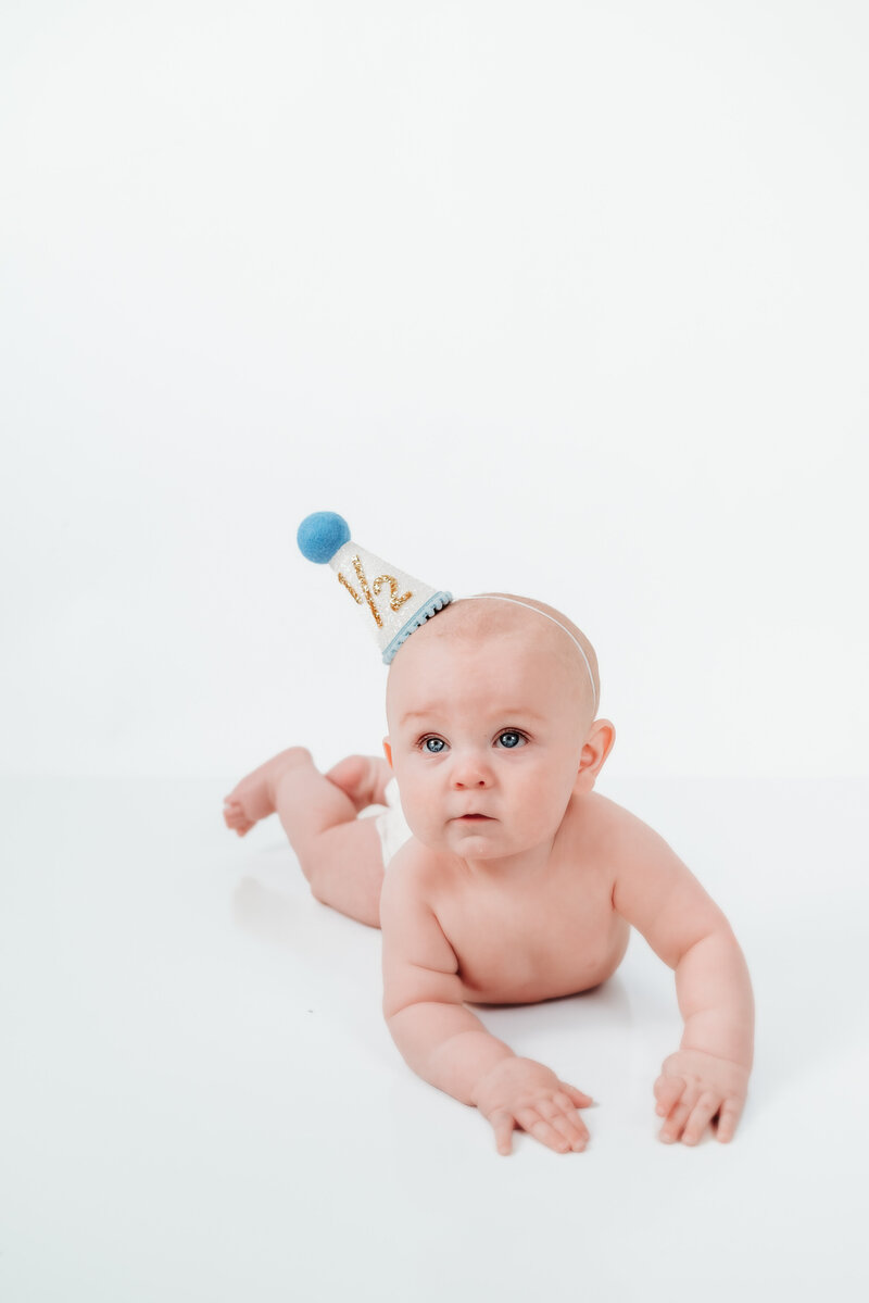 Baby boy lying on floor with 1/2 birthday hat.