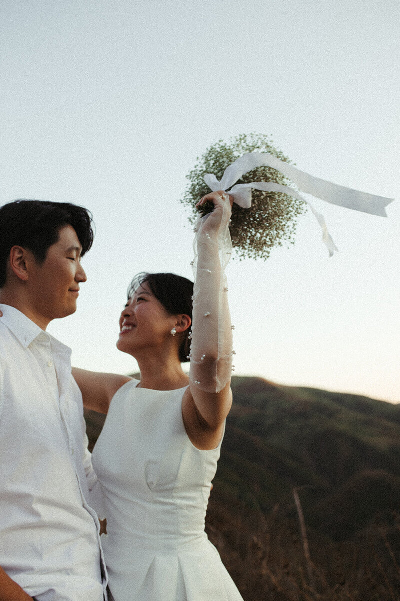 A bride and groom celebrate on their wedding day in Malibu. The bride throws her floral bouquet up in the air