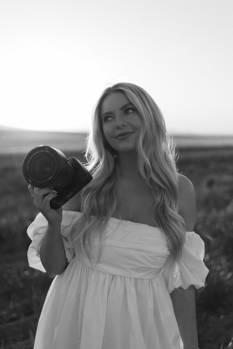 Wedding photographer in a white dress holding a camera.