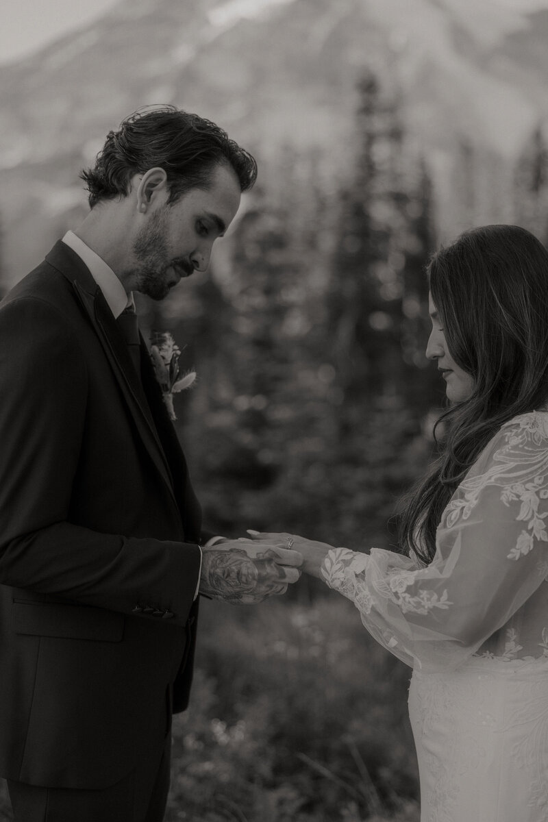 close up of groom putting ring on brides finger during elopement on mount rainier in washington state