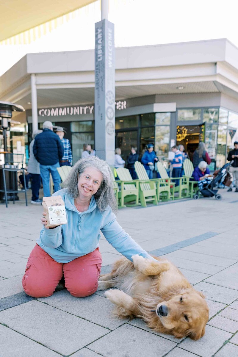 Woman kneeling and petting a golden retriever and smiling at the camera