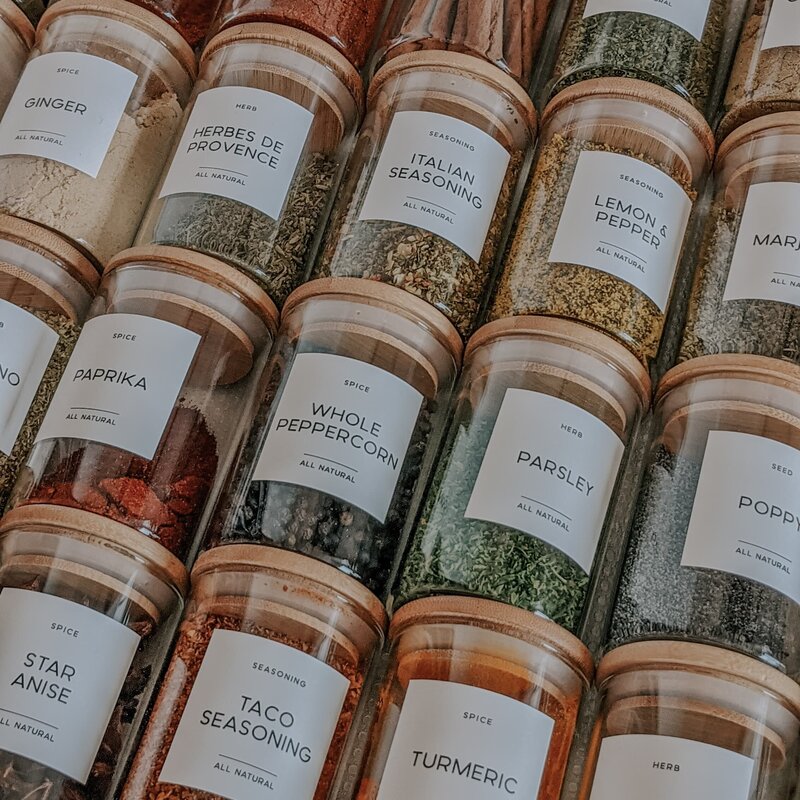 Colorful photo of glass spice jars neatly organized in a drawer, each with their own white minimal label