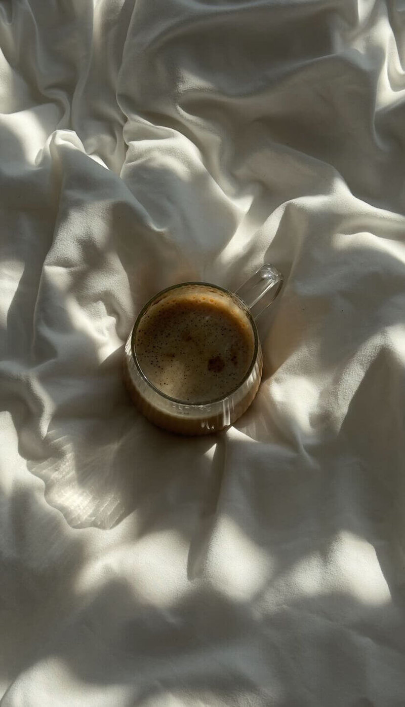 coffee in a glass mug on white rumpled bedsheets
