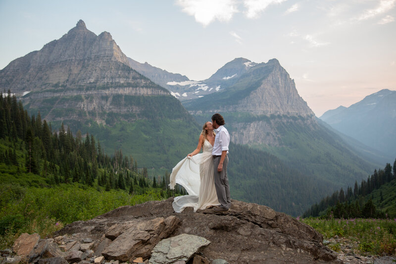 Bride kisses her husband in the fading light,  a deep mountain valley site behind them.
