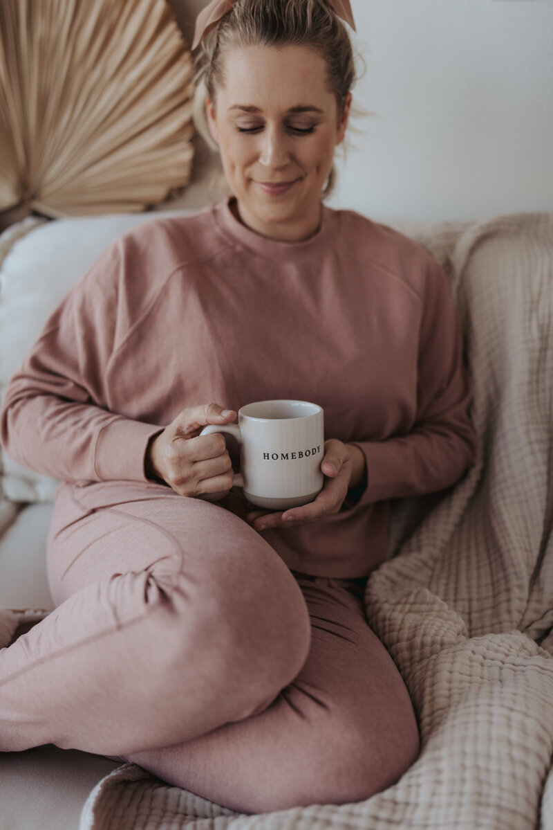 Sarah Kaetterhenry with Homebody coffee mug sitting on couch in sweatpants