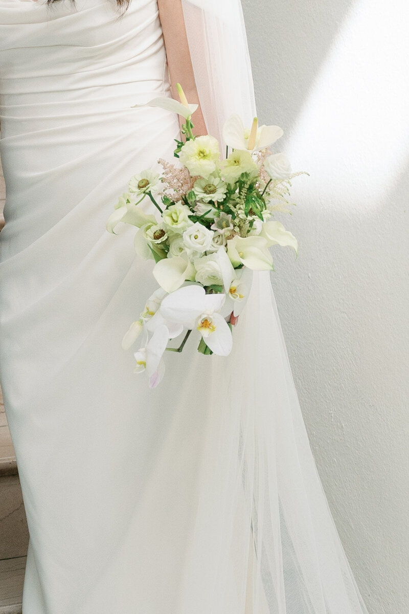 Close up of bride's arm holding white bouquet beside her dress