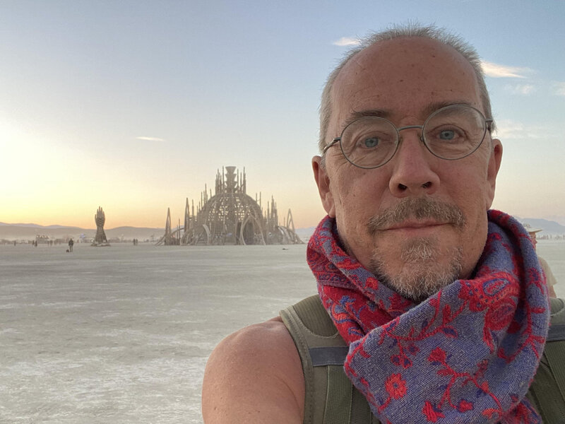 Robert Hildreth, a senior personal development and psychedelic prep coach, wearing a red and blue scarf with a serene sunset background.