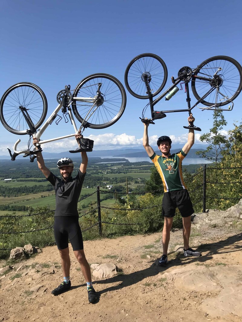 Jason Goldfarb with friend, they are both holding bikes above their heads in full cycling gear
