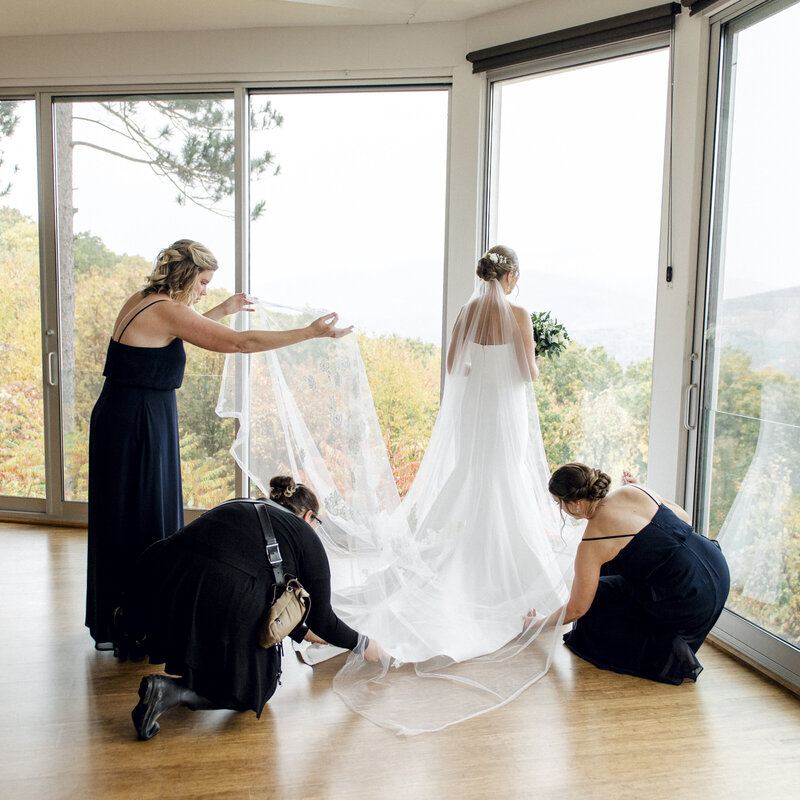 wedding photographer helps bridesmaids adjust the bride's dress and veil