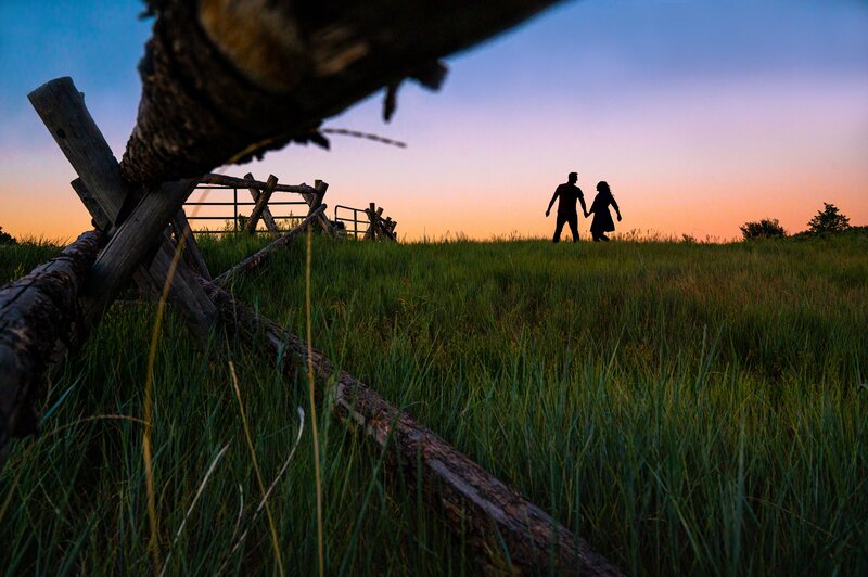 Couple silhouetted as they run across a mountain field at sunset.