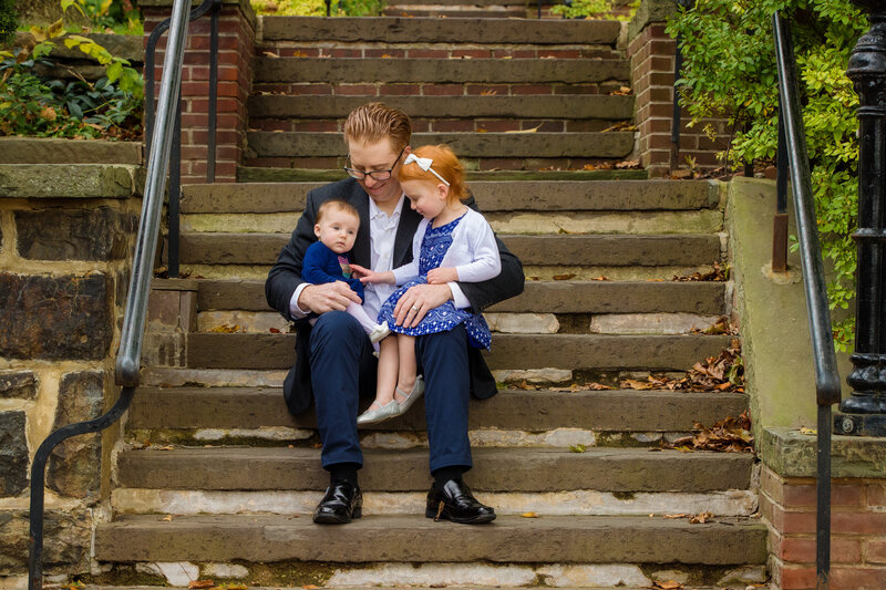 A father sitting on stone steps with his two children, captured during a mini session in Bethlehem, perfect for family photography