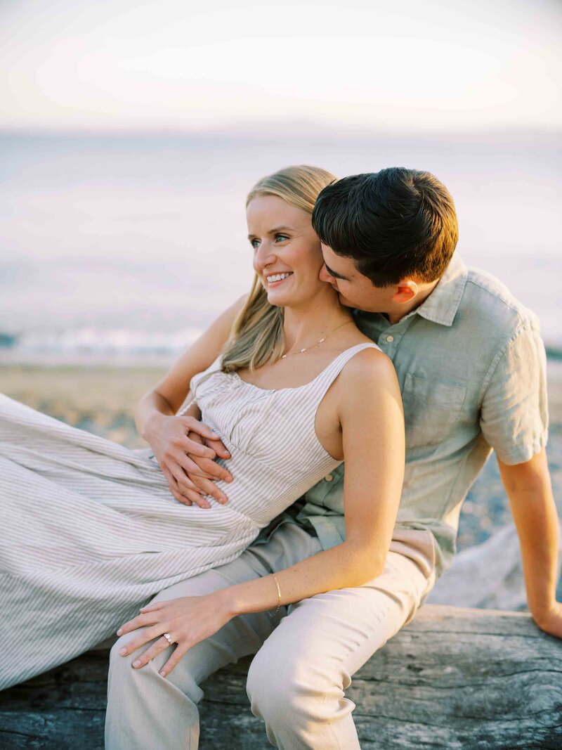 seattle engagement photographer captures engaged couple sitting on beach log at sunset on film