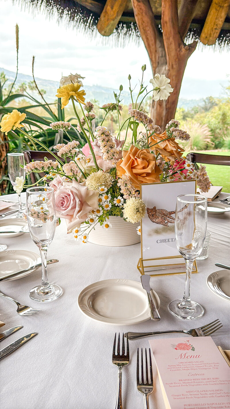 Reception tablescape featuring wild orange and pink florals and table numbers with zoo animals on them at San Diego Safari Park in Escondido, California.