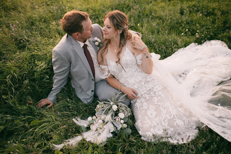 A wedding couple leaning into each other as they sit in the grass.