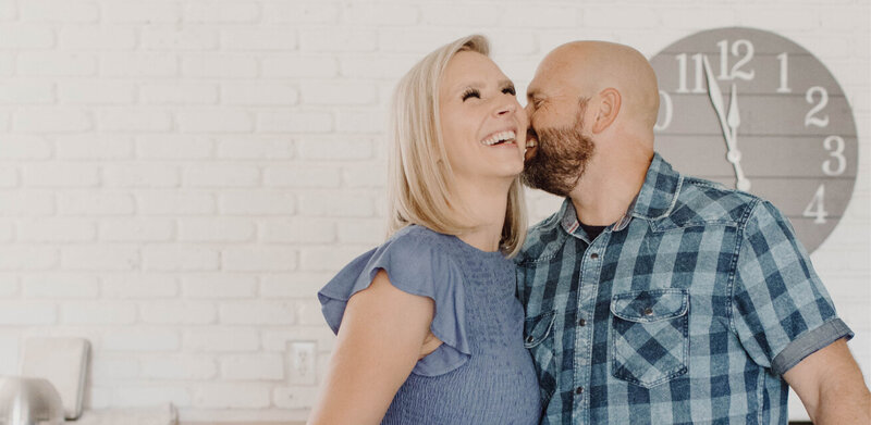Leslie is giggling while her husband kisses her cheek