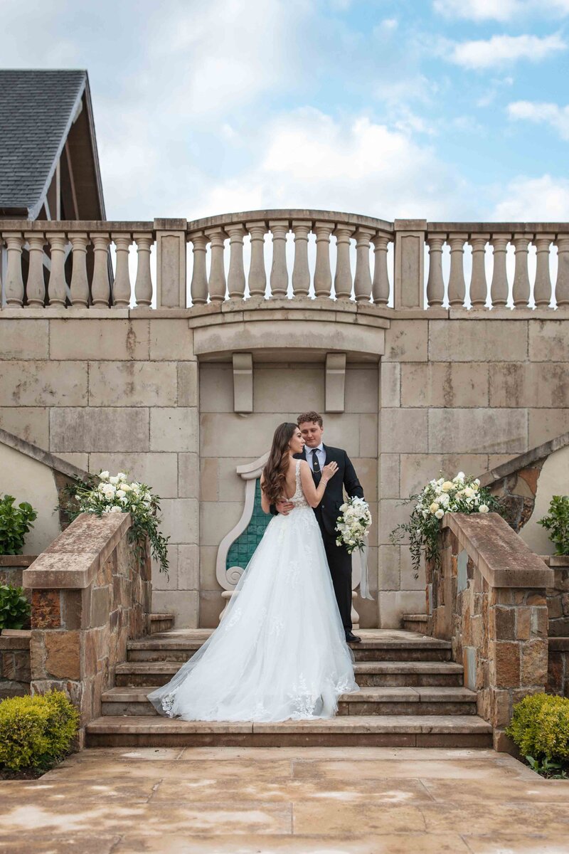 a woman in a lace wedding dress hugs a man in a black suit at the Chateau De Lis in Oregon City, OR