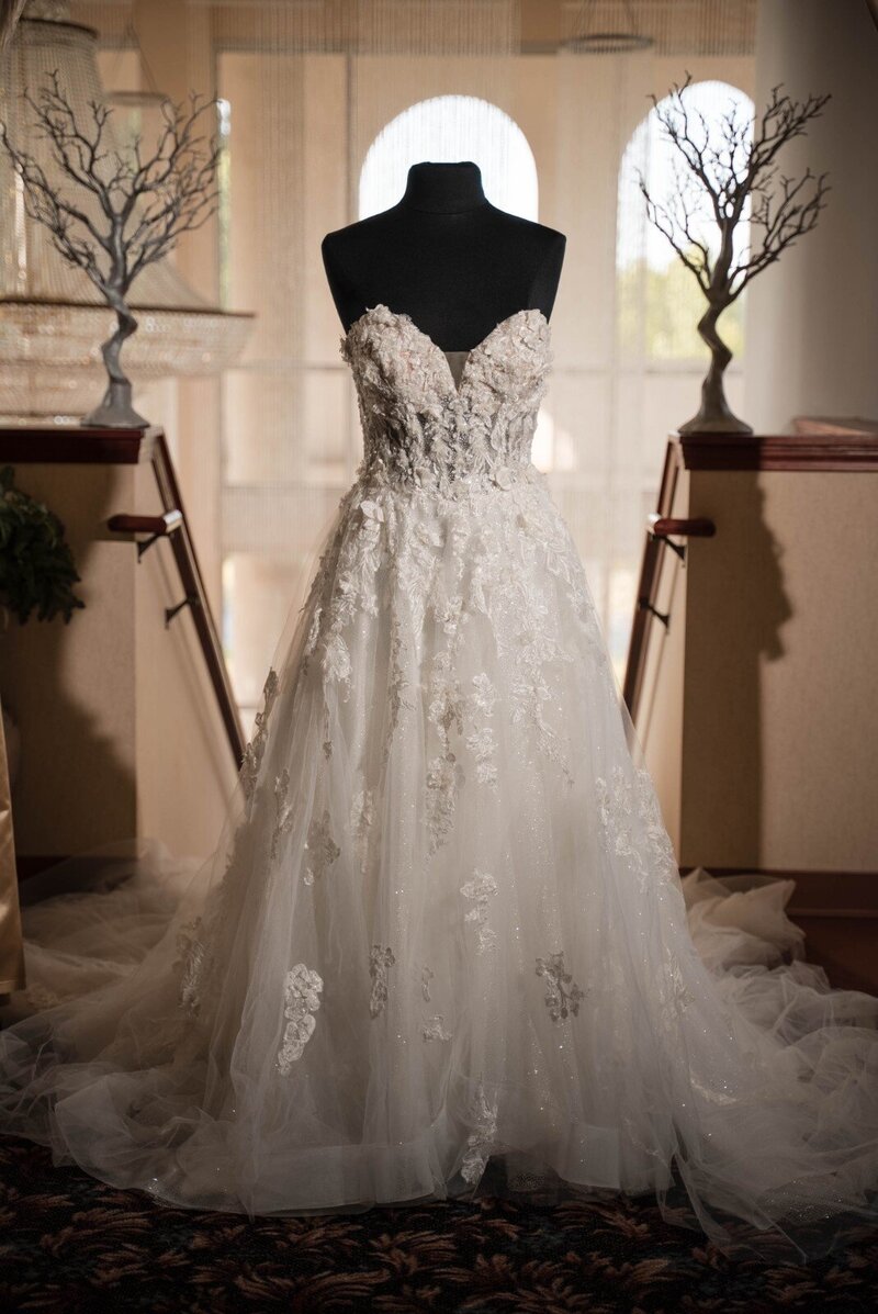 Detailed lace wedding dress displayed on a mannequin by the staircase at Duneland Falls Banquet Center.