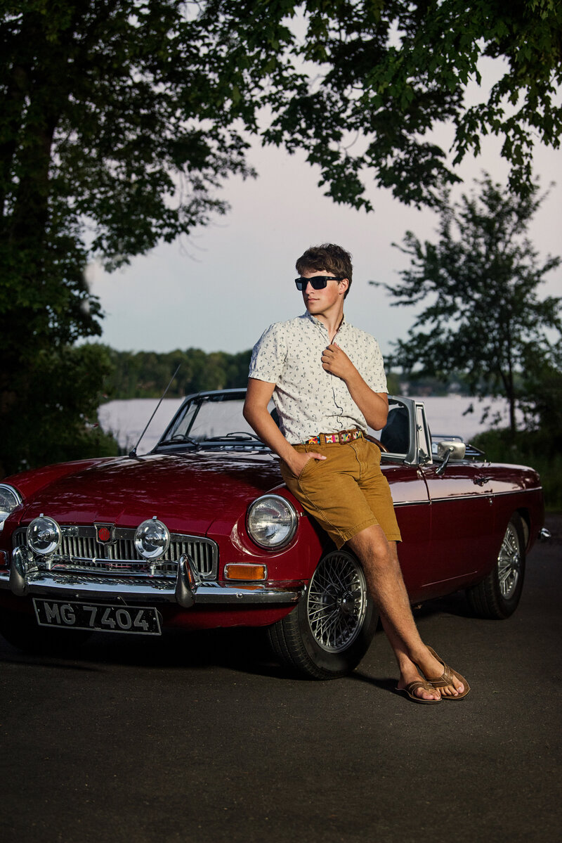 high school grad photo of boy with vintage car and sunglasses against Lake Minnetonka
