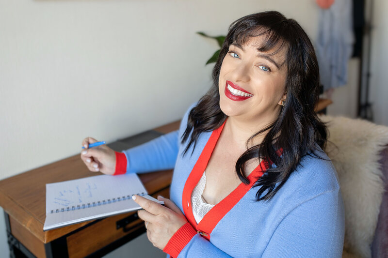 Wedding industry educator, Renee Dalo, smiles for photo in blue cardigan with red trim