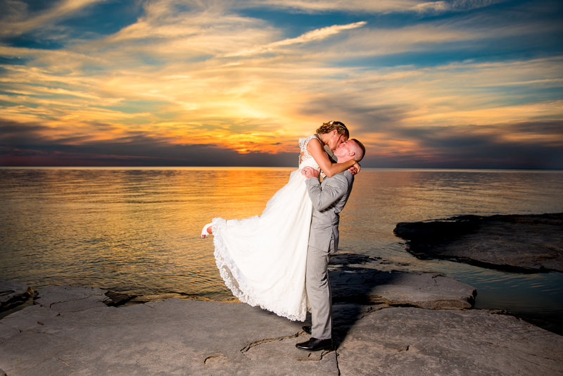Groom lifts bride during a vibrant sunset for a photo