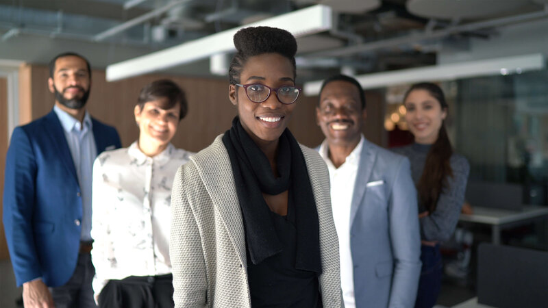 Confident businesswoman in glasses standing with her diverse, smiling team.