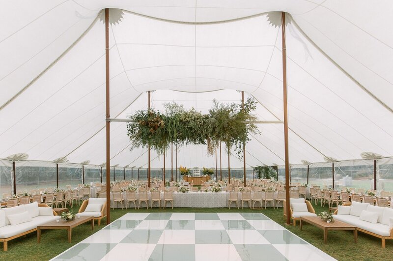 Green and white wedding decor, custom checkerboard dance floor, hanging floral installation, lounge set up, and dining tables set up under a sailcloth tent on the lawn at Ojai Valley Inn in Ojai, California