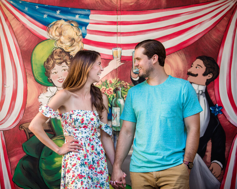Couple standing proudly in front of a mural featuring an American flag, creating a patriotic touch to their engagement photos.