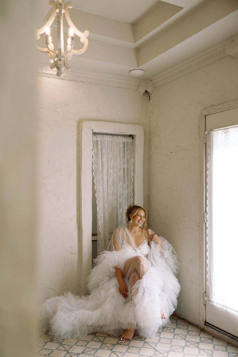 Bride and groom share a quiet moment on a leather sofa beneath a sunlit window — refined and modern wedding portrait captured by Kelly Lugo Photo.